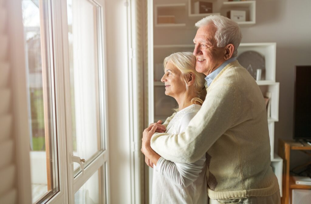 Elderly couple looking out the window smiling standing in their new senior home