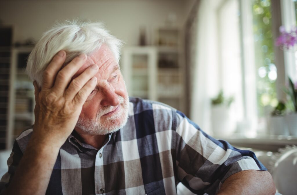 A male senior citizen with his hand on his head, looking out the window